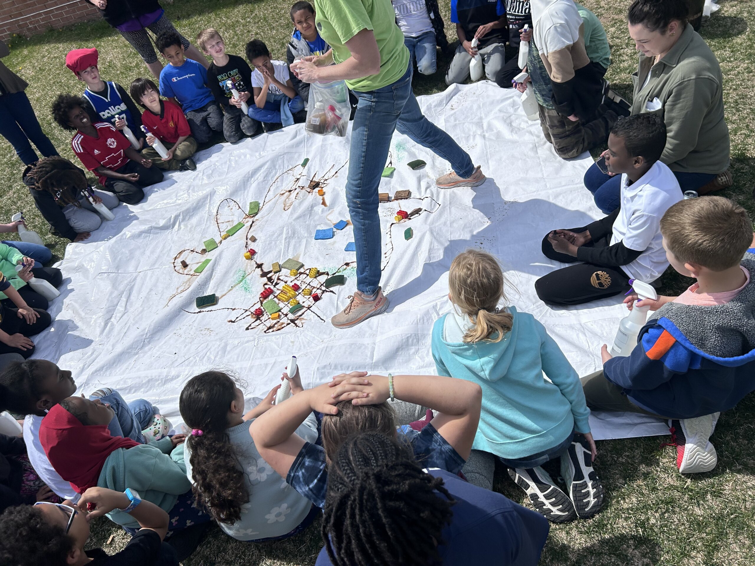 a group of elementary students surrounding a plastic tarp on the ground for a watershed classroom activity that shows runoff. 